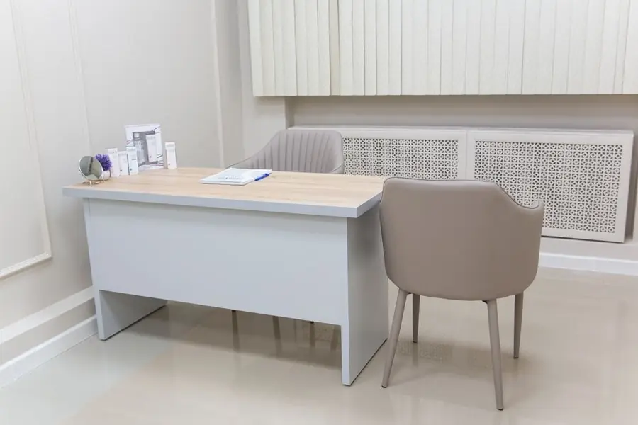 Empty modern clinic consultation room with desk and treatment chair