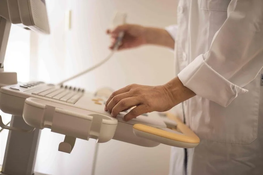 A clinician's hands adjusting the control panel of an ultrasound treatment device