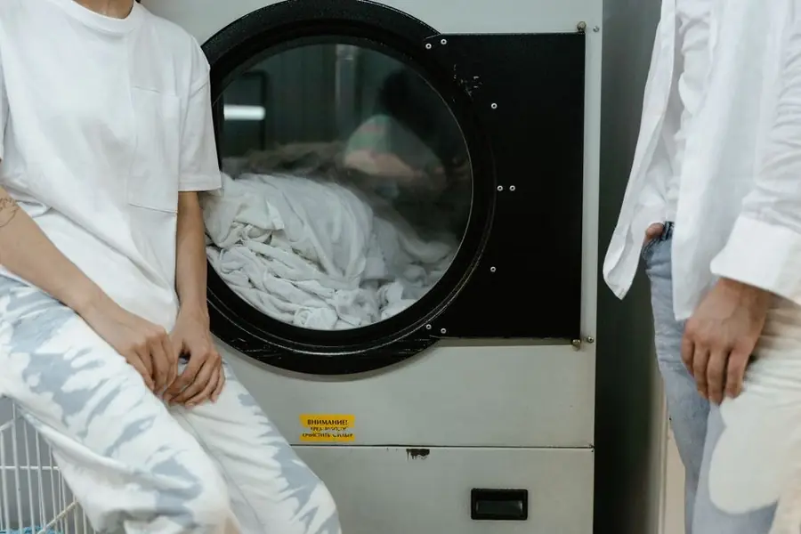 明るいランドリールームで、薄い色の服を着た二人が洗濯機に洗濯物を入れている様子