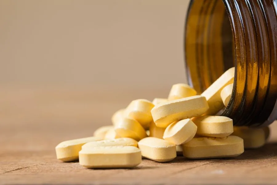 Tablets and capsules spilling from an open supplement bottle onto a wooden table